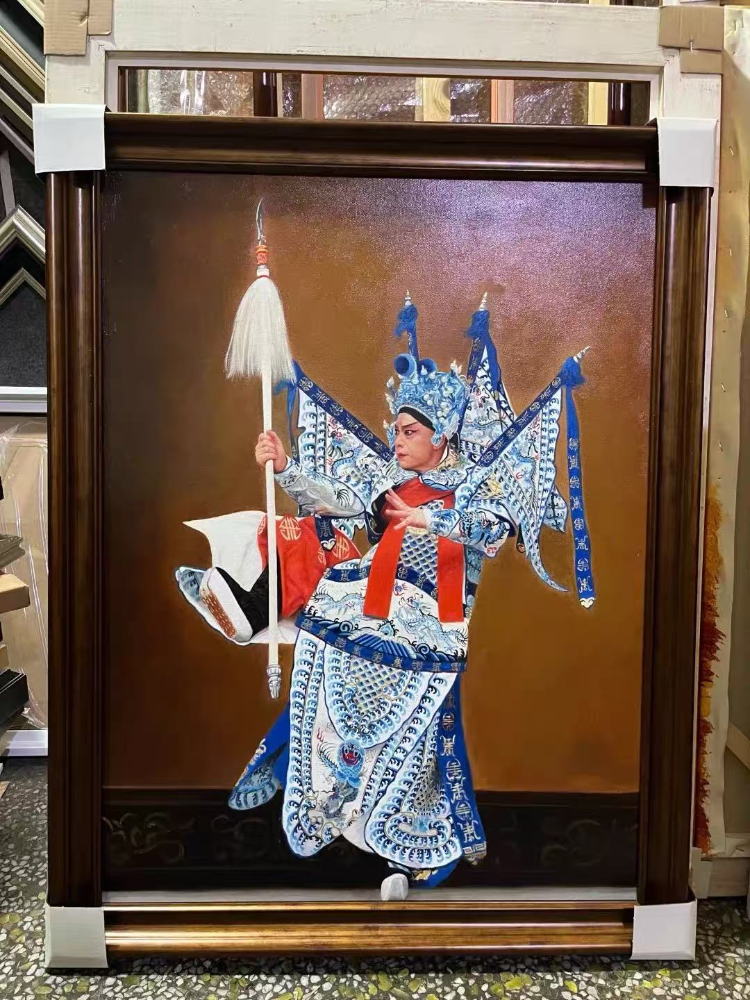 一幅有框的中國戲曲演員肖像,演員身穿藍白華麗戲服、頭戴戲曲冠飾,背插靠旗並手持長桿兵器。