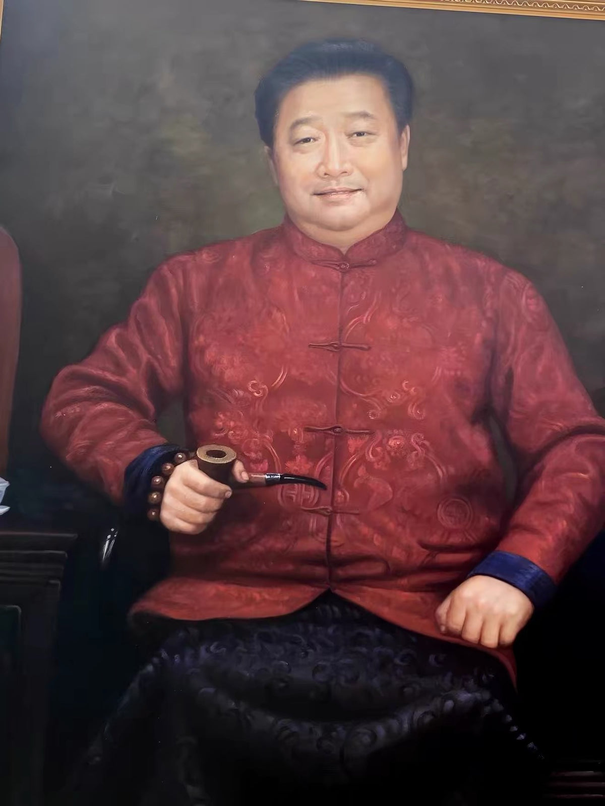 Retrato formal sentado de un hombre de mediana edad con chaqueta tradicional china roja y una pipa sobre un fondo gris parduzco oscuro.
