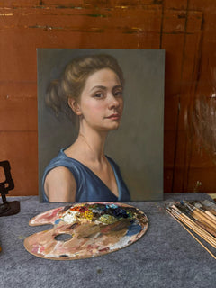 Classical painted portrait of a woman in a blue dress displayed in an artist's studio